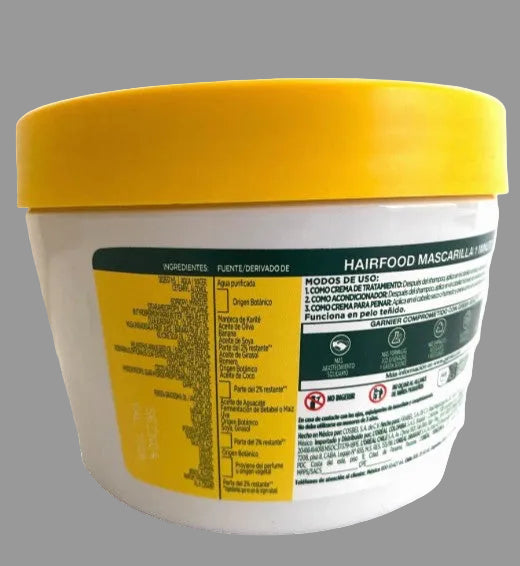 A white plastic tub of hairfood mask with a bright yellow lid, showing the Spanish side label with ingredients and usage instructions.